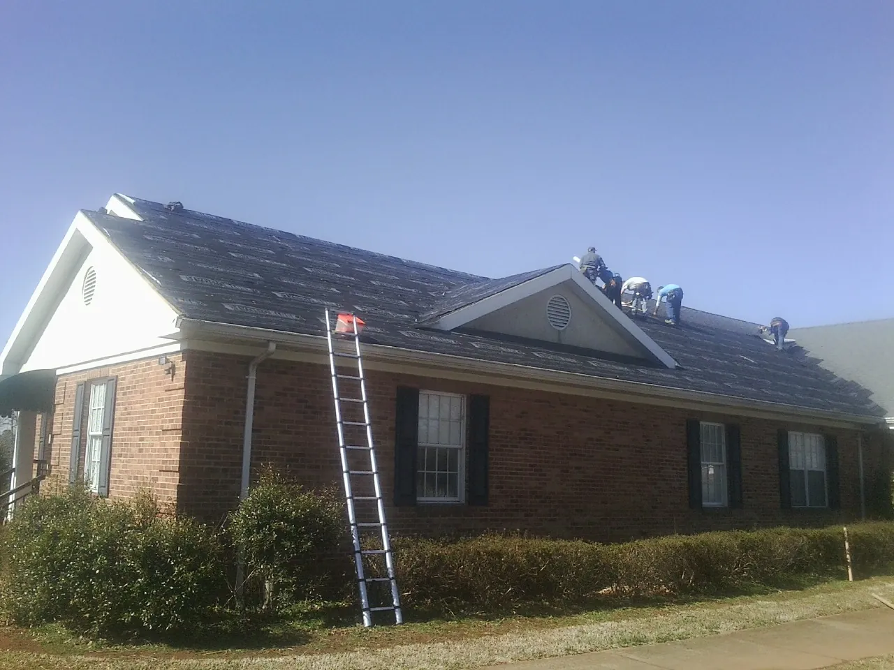 Crew tearing shingles off a brick ranch roof with a ladder set — Metal Roof Repair work by our crew in Helena