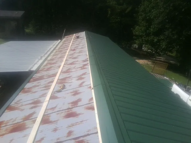 Old rusted panels beside newly installed green metal roofing — Wind Damage Roof Repair by Roofing Brothers in Helena