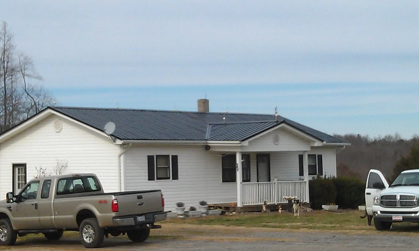 Finished dark metal roof on a white ranch home with work trucks parked in Helena