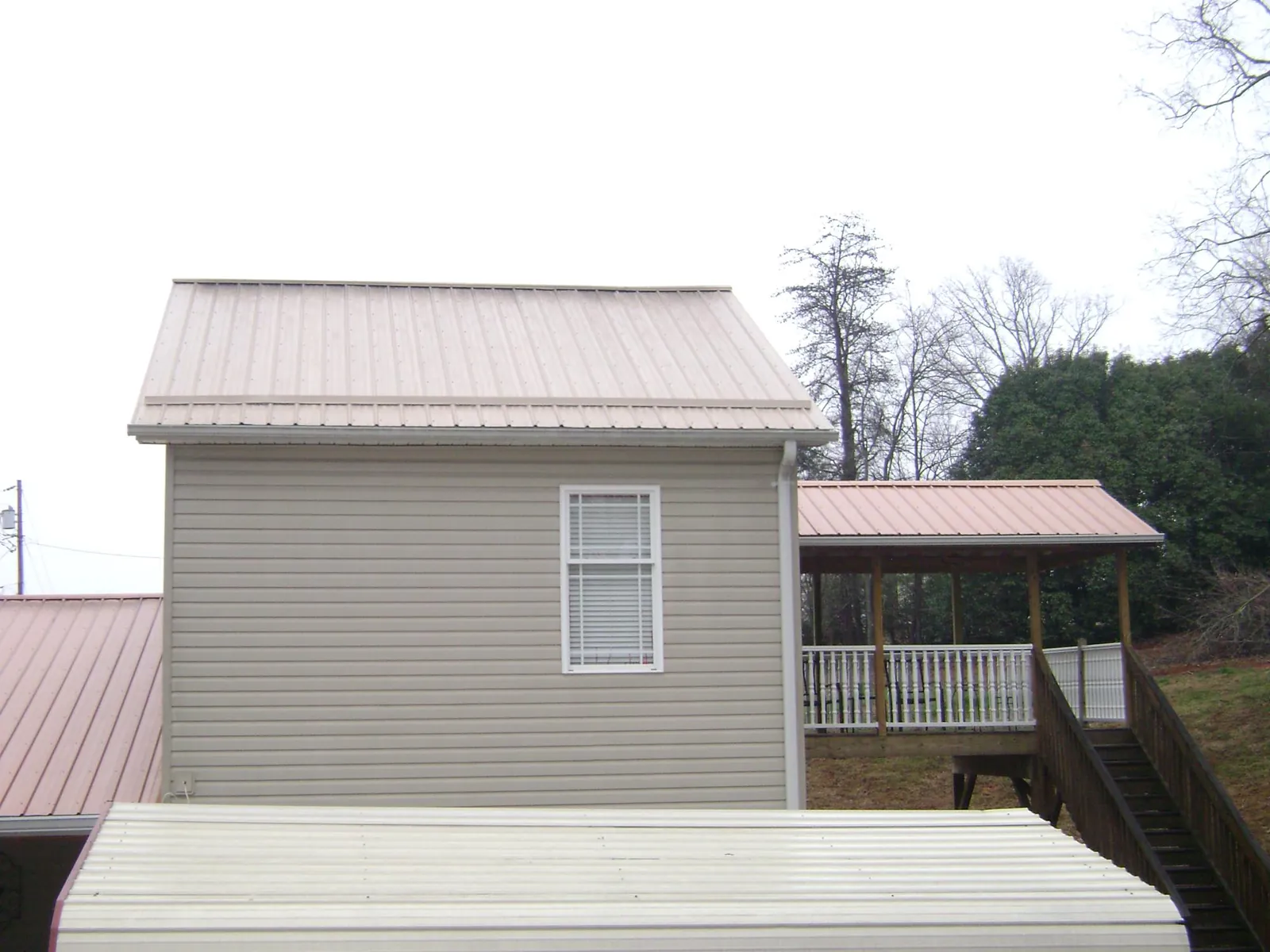 Tan metal roofs on a two story addition and attached porch, from a Roof Replacement job in Helena